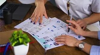 Hands reviewing printed website wireframe sketches on a desk